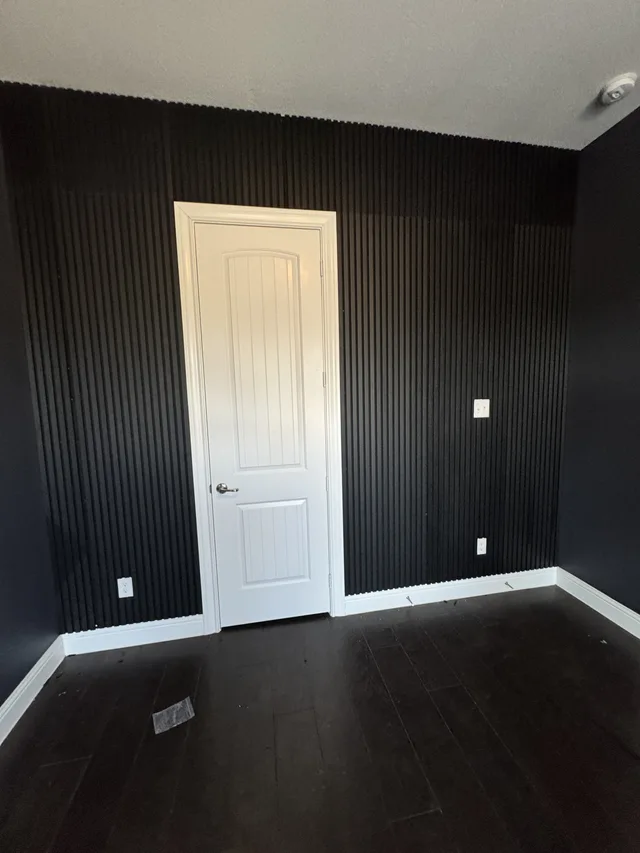 Dark vertical wall panels installed around a white interior door, outlets, and a light switch