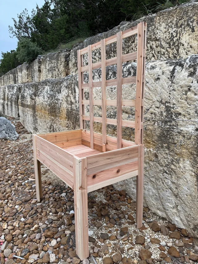 Raised cedar planter on four legs with an upright trellis beside a stone wall