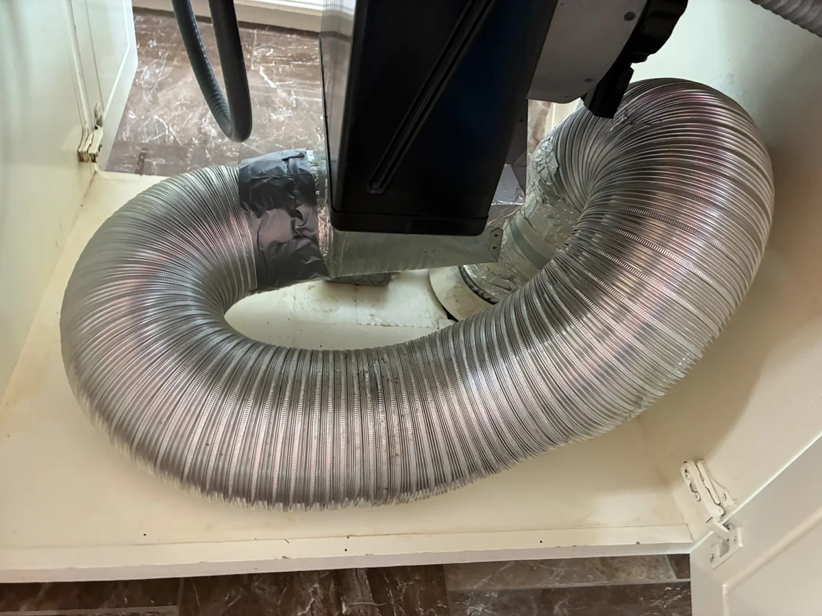 Old flexible metal downdraft duct looping beneath the same stovetop before replacement