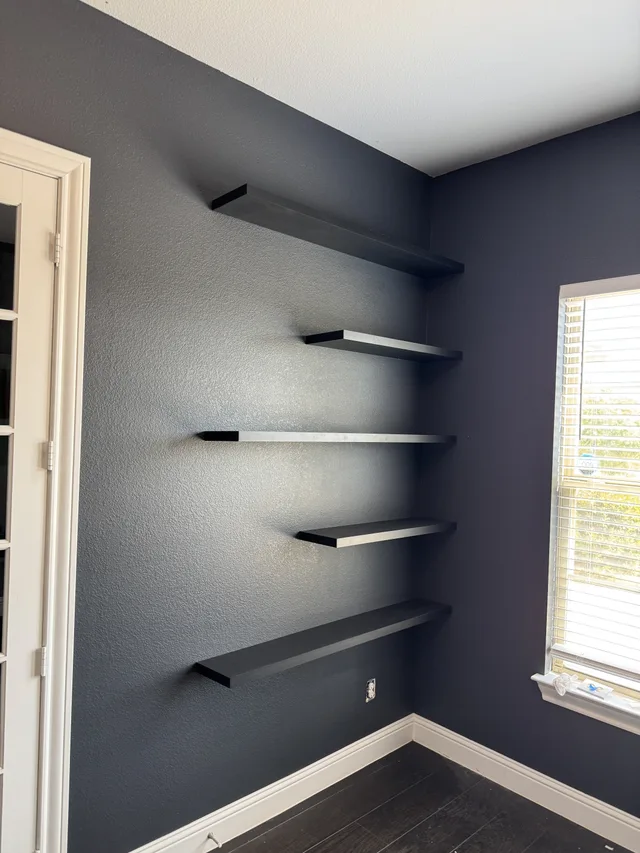 Five dark floating shelves installed in a staggered arrangement on an interior wall