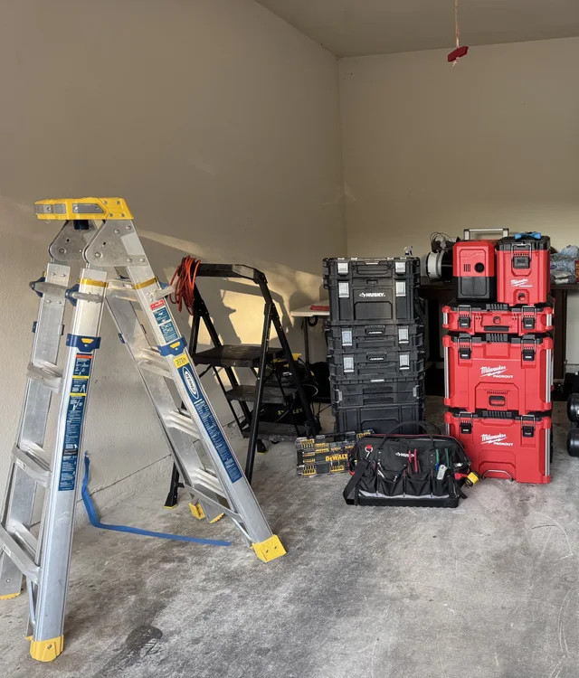 Ladders, stacked tool storage, and a tool bag arranged in a garage